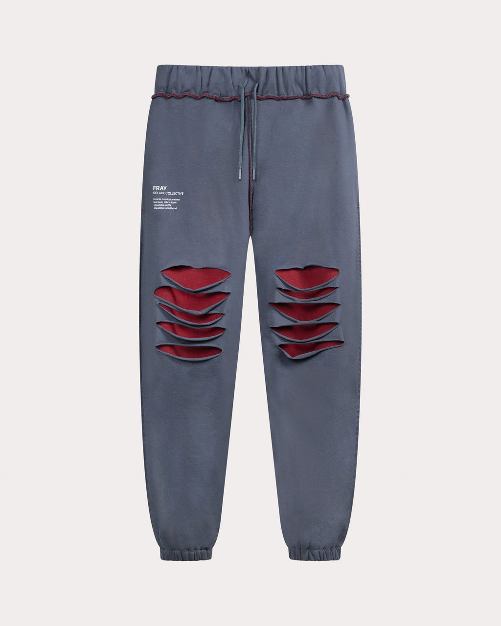 The image shows the FRAY sweatpants in blue from SOLACE Collective, featuring layered cut-out panels at the thighs that reveal a contrasting red underlayer. The design includes an elastic waistband with a drawstring, elastic ankle cuffs, and printed branding on the upper left leg for a bold, structured look.
